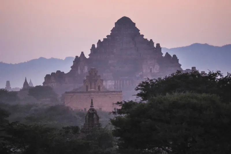 A temple in the background with foggy red sky and trees in front in Bagan - one of the best places to visit in December