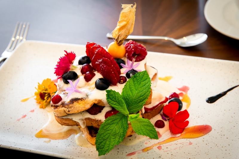 Pile of French Toast decorated with flowers, mint leaves and red berries
