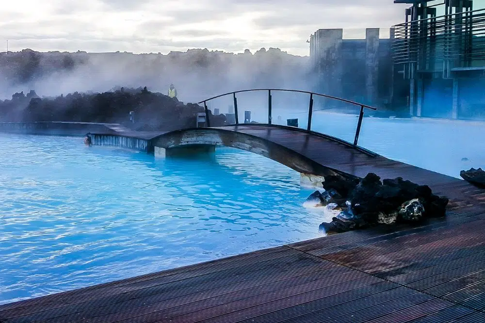 Blue water outside with lots of steam and bridge splitting two pools