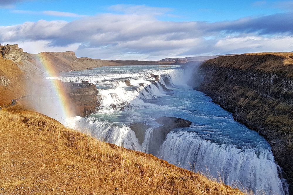 Gullfoss waterfall with yellow grass surrounding and a rainbow on the left